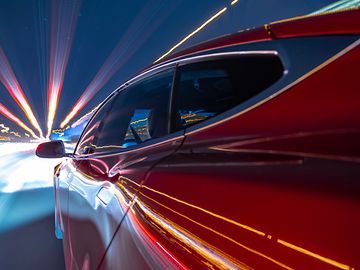 A red car drives towards lights at night