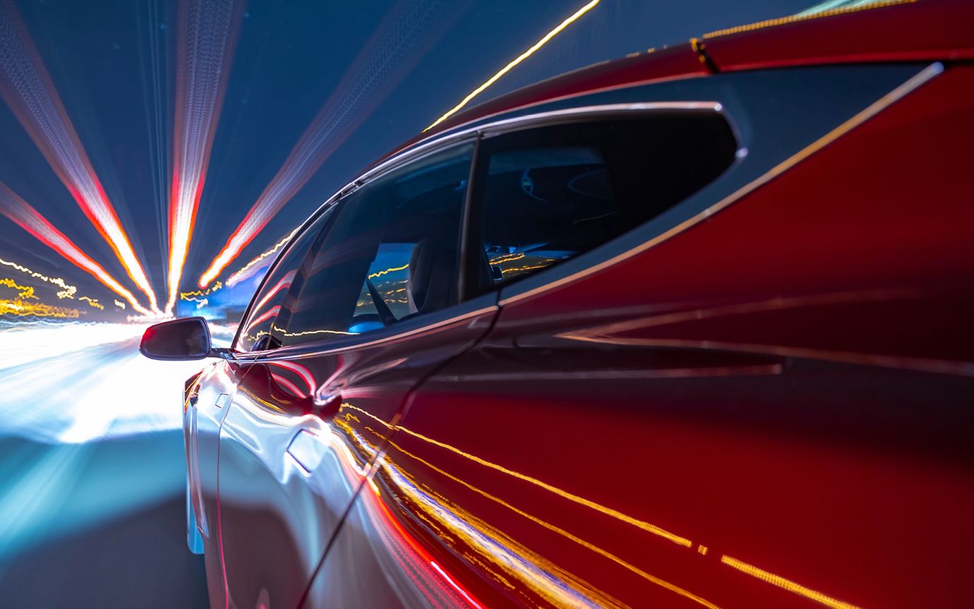 A red car drives towards lights at night