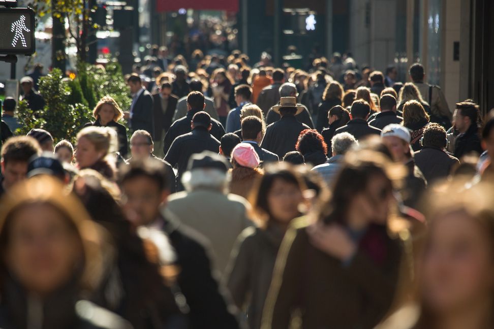 People walk on the sidewalk of a main thoroughfare in a major city