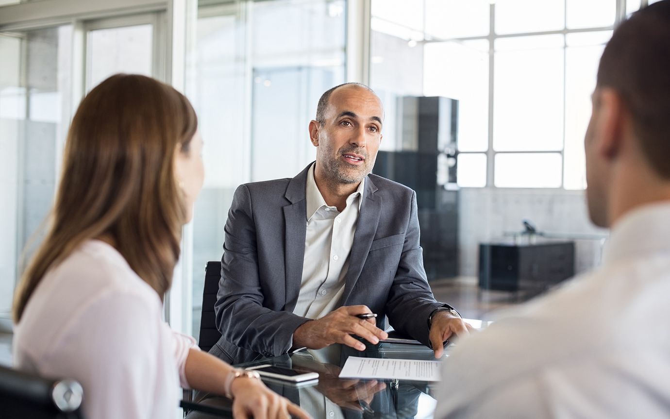 Man with pen and notepad talking to two people in an office environment