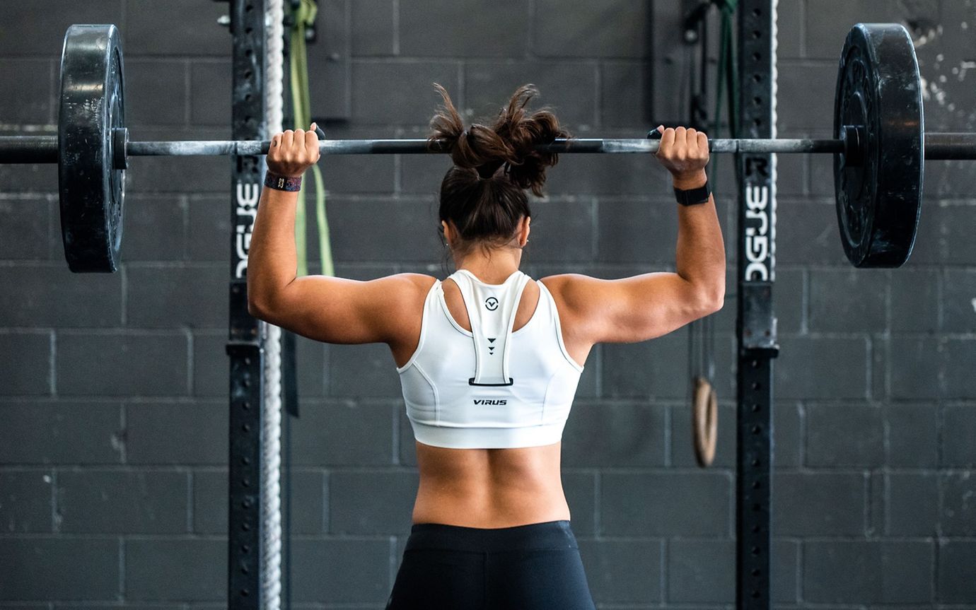 A person in sportswear in a gym lifting a barbell with heavy weights over their shoulders