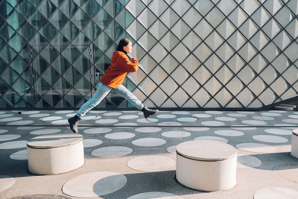 A person jumps from one low pillar to the next in an urban environment