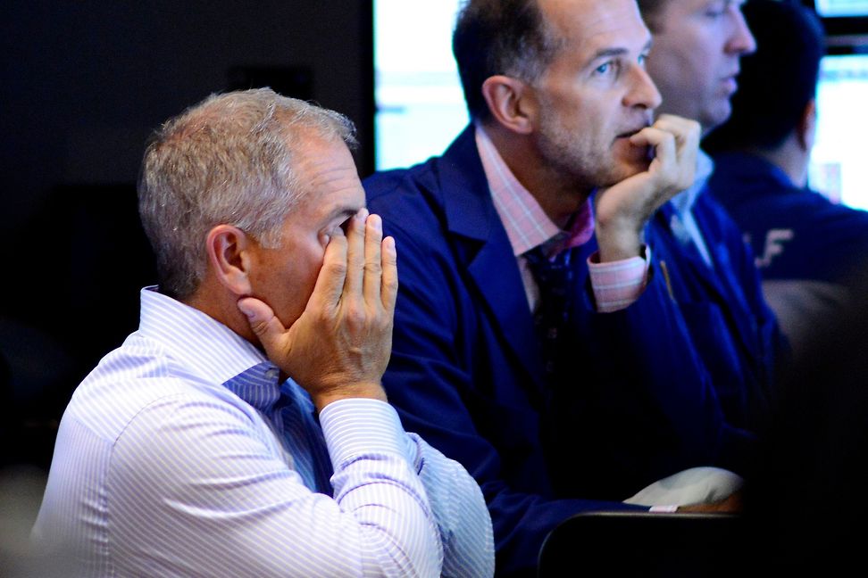 A trader buries his face in his hands while another looks on worriedly