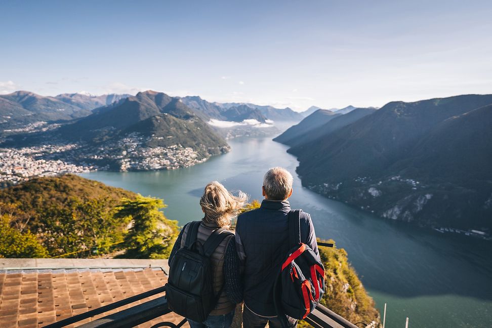 Two walkers, seen from the back, looking down from a hill onto a lake