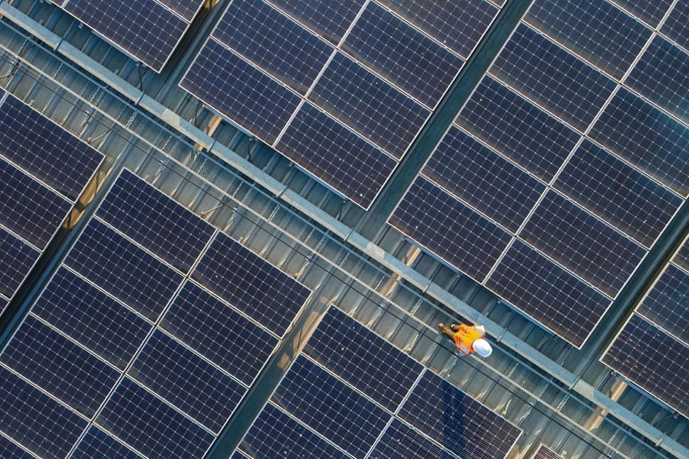 Worker with helmet on the roof walking by lots of solar panels