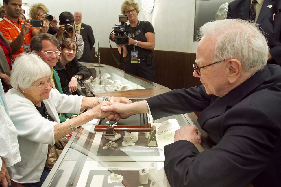 A woman smiles as she shakes hands with an older man in front of an audience