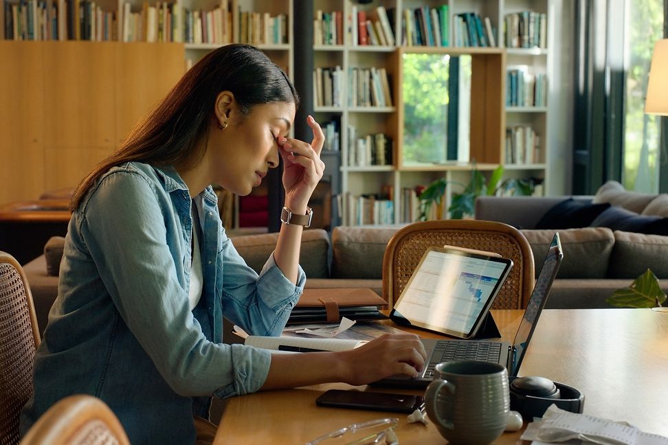 A woman leans her head in her hands, looking exhausted and desperate as her laptop waits for another use.