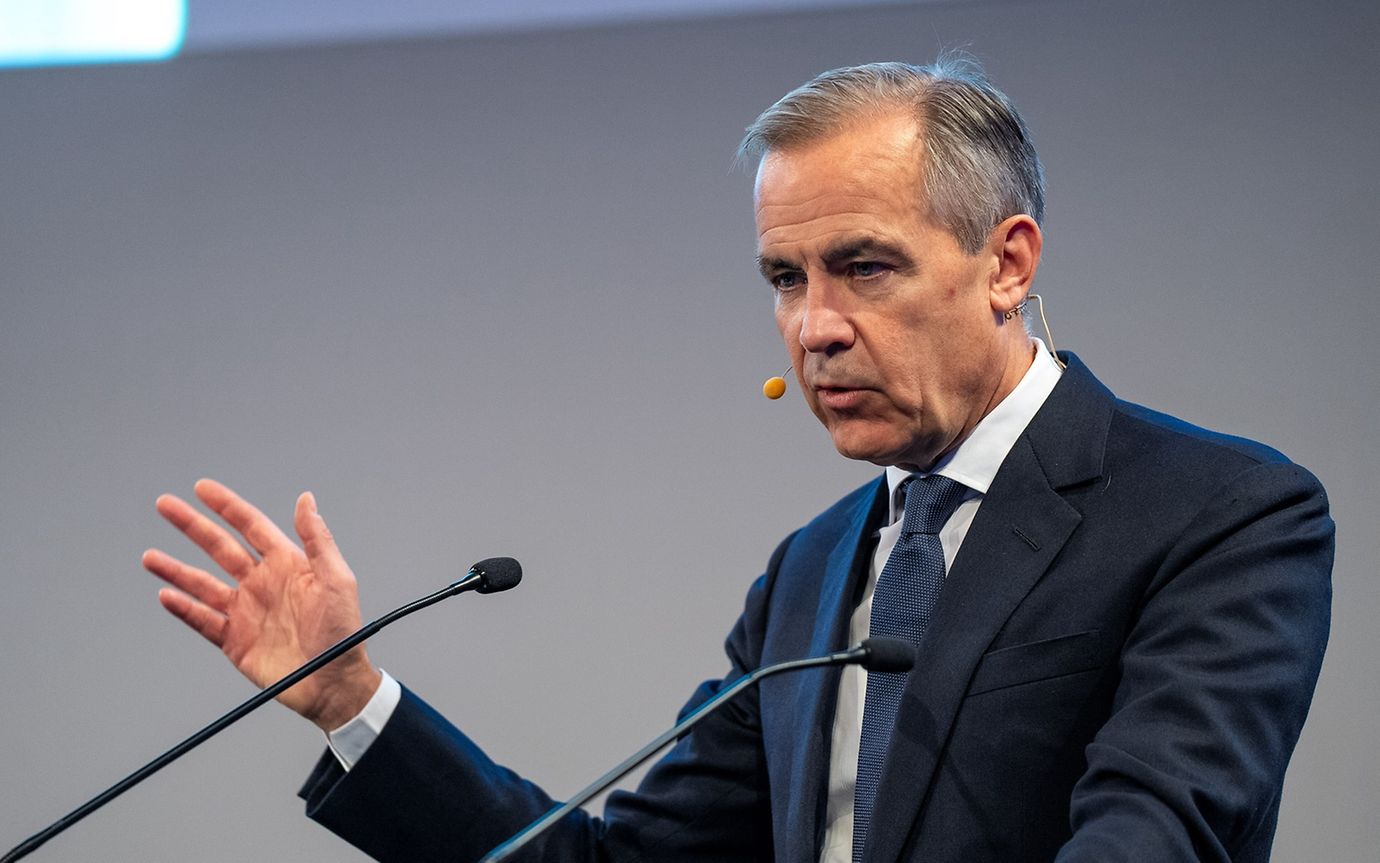 A man in a suit and tie speaks into a microphone and gestures with his hand.