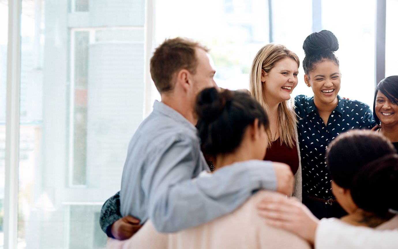 A diverse group of young people in a modern office building are standing in a circle.