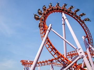 People are turned upside down in the loop of a giant rollercoaster, set against a blue sky.