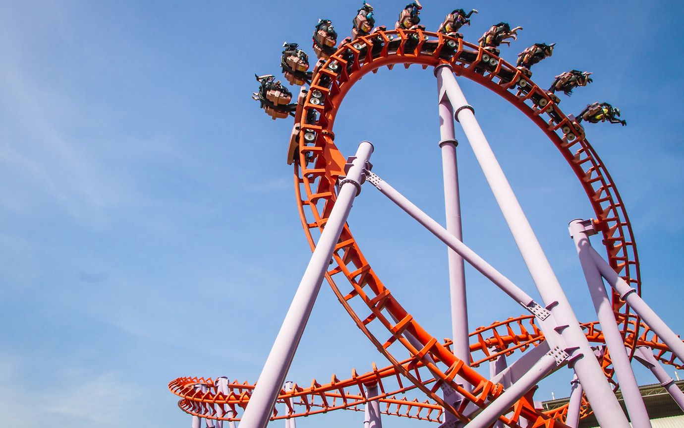 People are turned upside down in the loop of a giant rollercoaster, set against a blue sky.