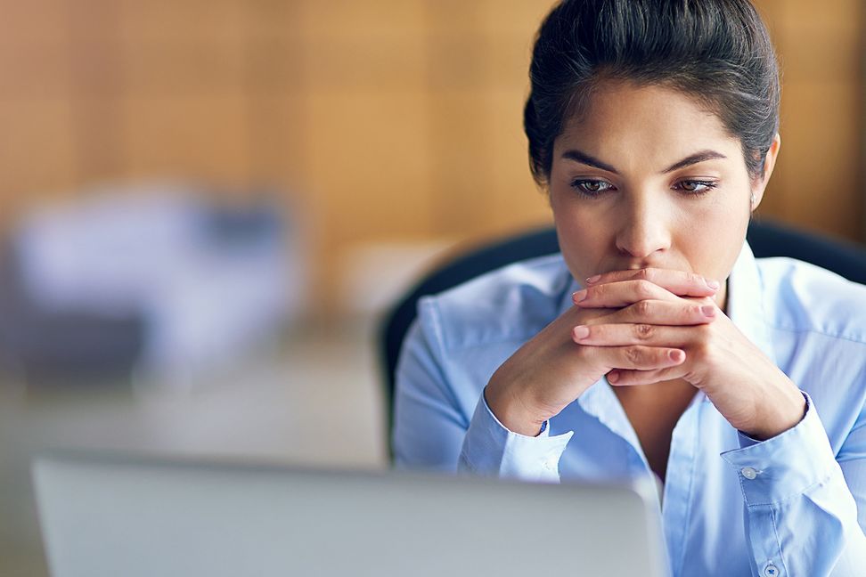 A woman looks at a screen, her hands folded under her chin, a little worried and thoughtful.