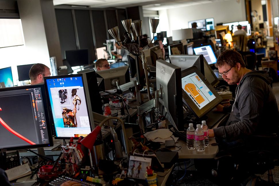 Young employees stand at desks with many monitors in a sparsely lit office.