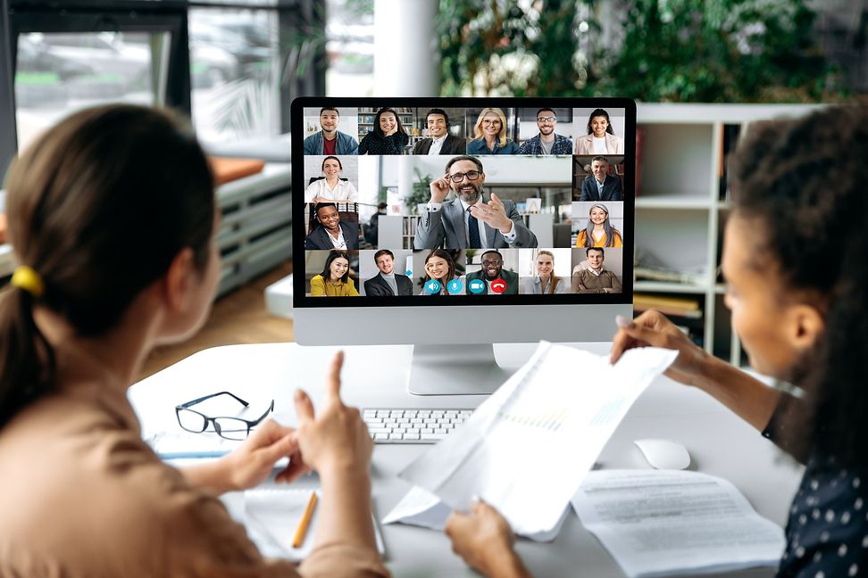 Two employees look at a screen displaying photos of many people taking part in this virtual meeting.