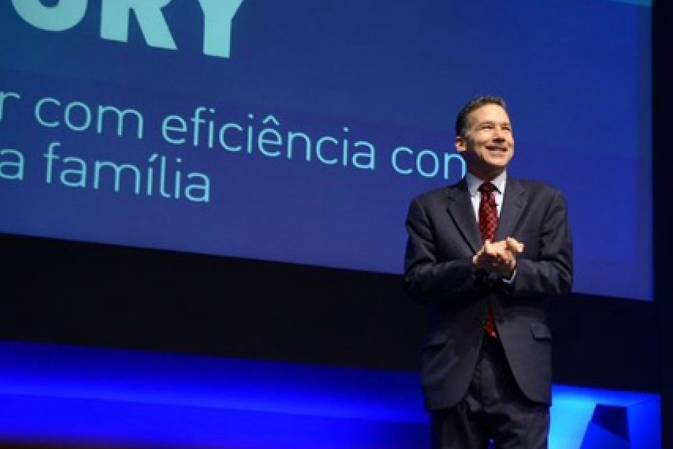 Middle-aged man presenting on a large stage in front of a blue screen.