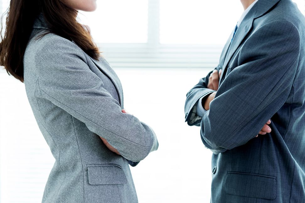 Woman and man in a suit stand facing each other with their arms crossed. The cut shows only the torso - without heads.