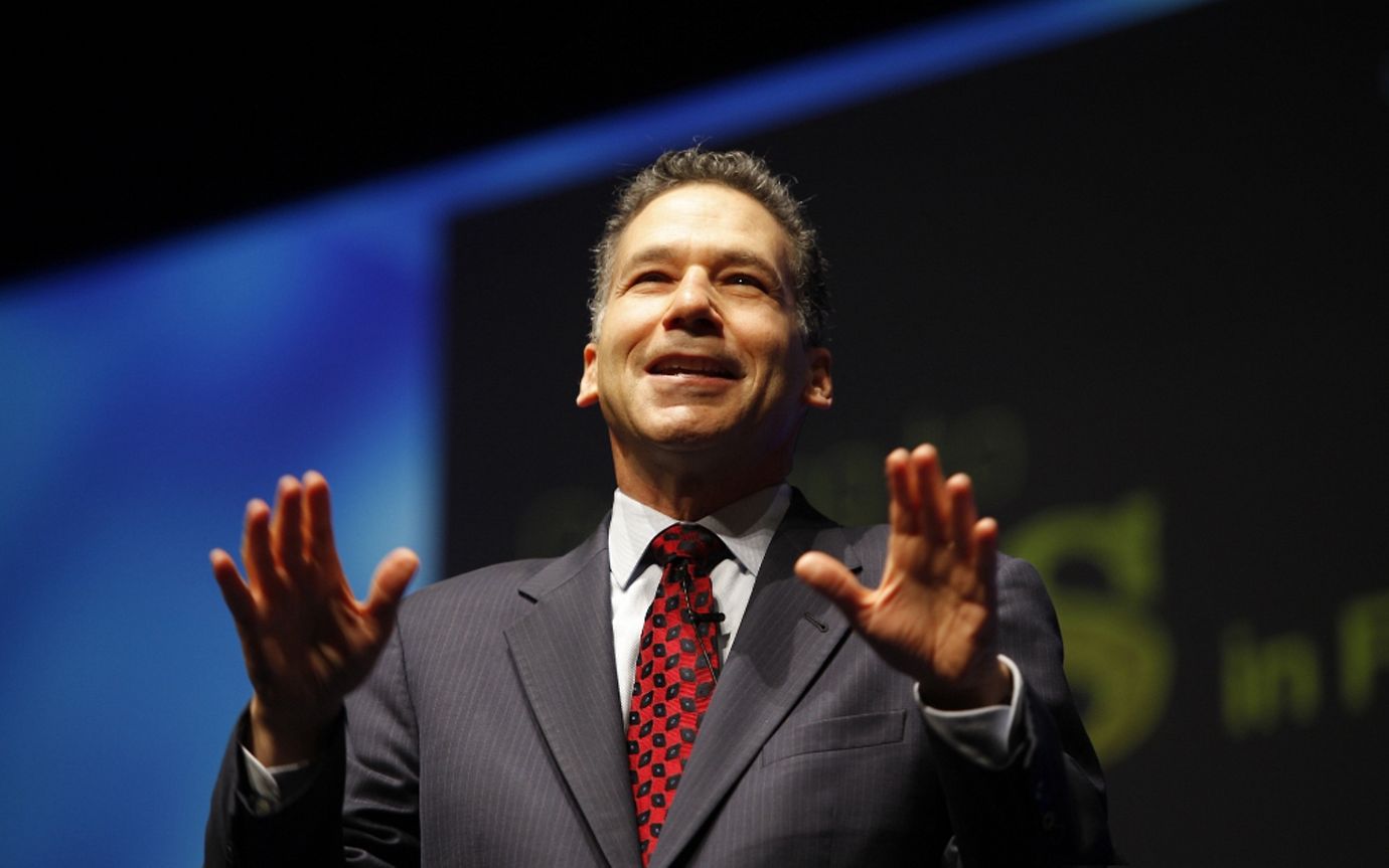 Middle-aged man smiling on a dark stage with outstretched arms