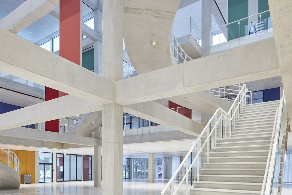 Modern, bright architecture of a large hall, white supporting beams and a staircase are visible. 