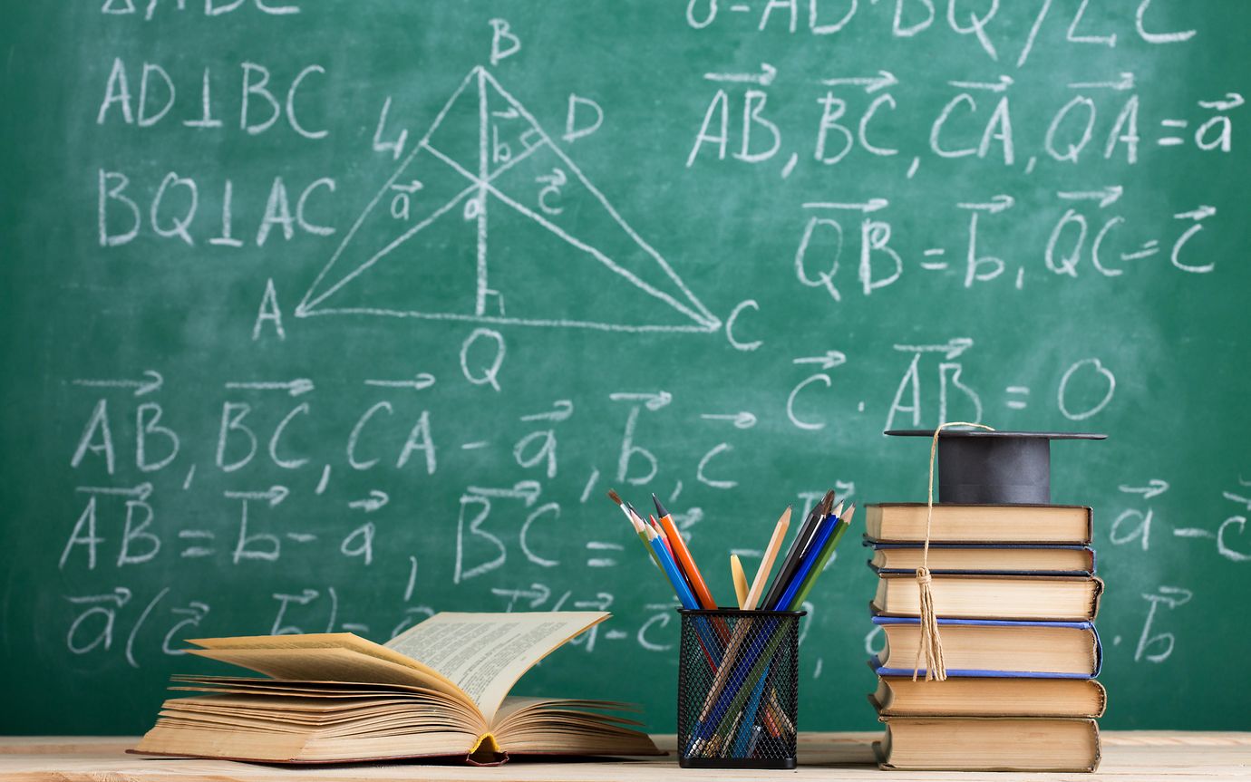 Chalkboard with books, pen pot and graduation cap on the desk.