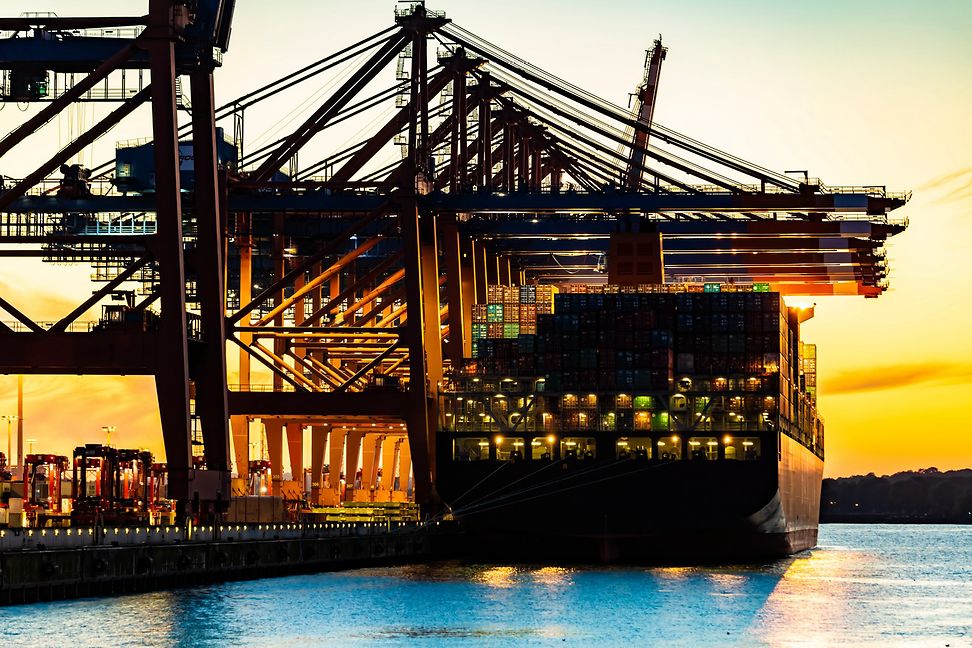 A container ship in the harbour is being loaded at sunset.