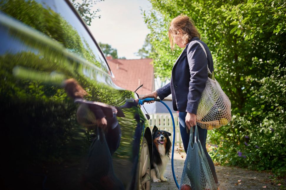 A person refuelling a car, with trees and houses in the background.