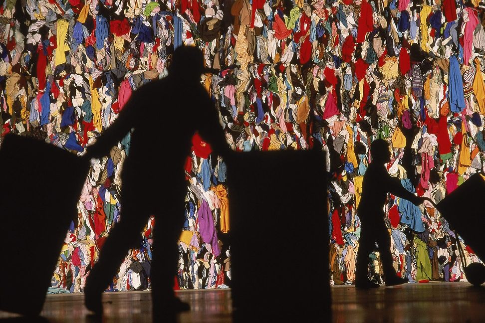 A man pushes two tonnes in front of a mountain of textiles.