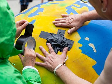 Two activists stick a plaster on a balloon that looks like an earth.