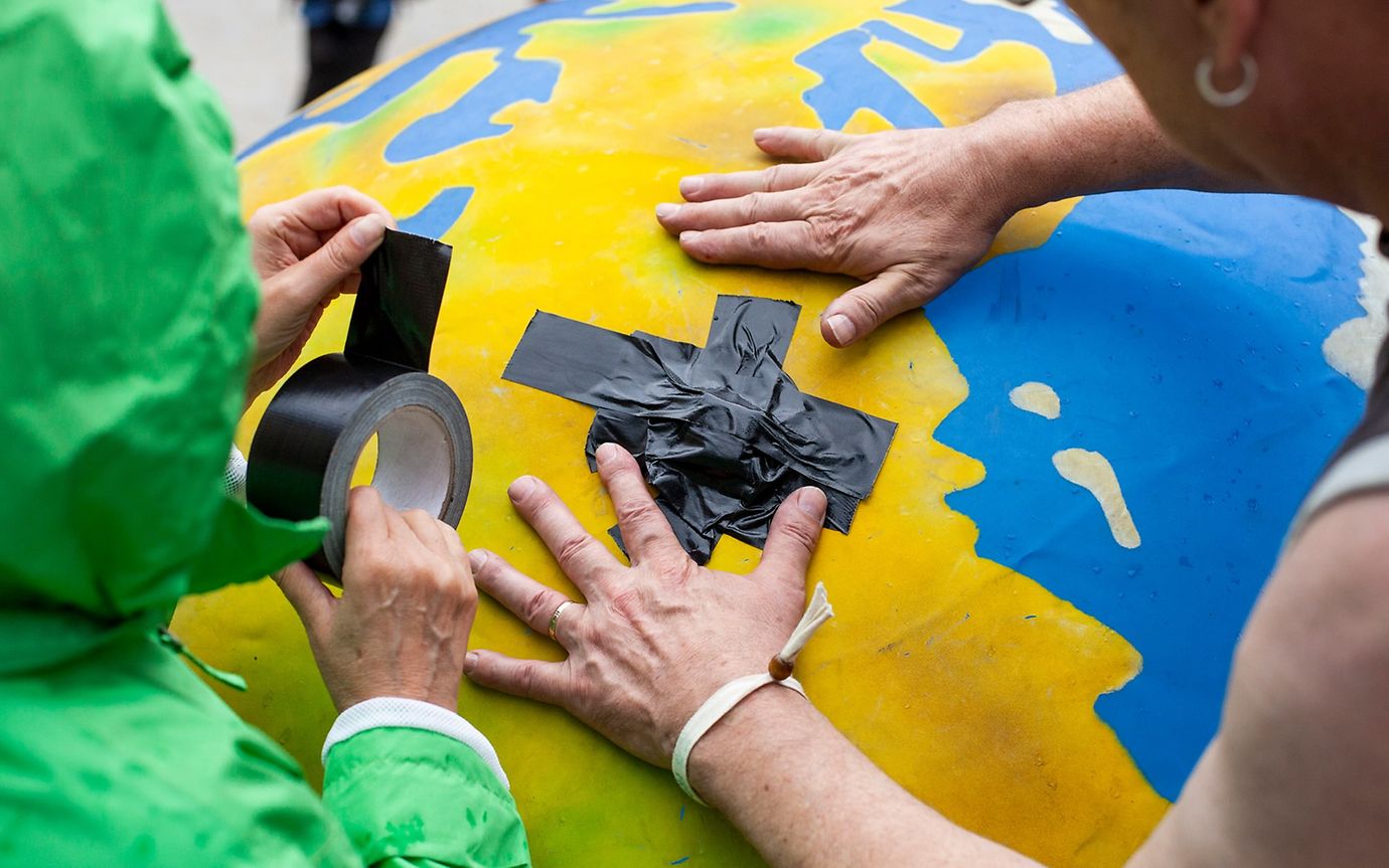 Two activists stick a plaster on a balloon that looks like an earth.