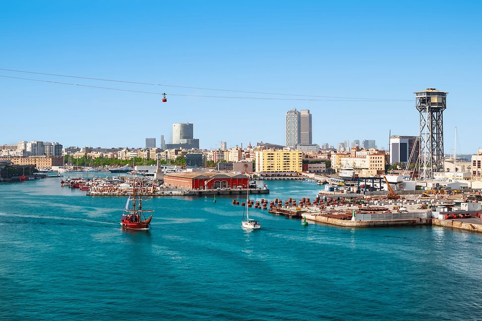 The viewer looks out over a large expanse of water towards a harbour and a city beyond. A cable car is visible in the sky.