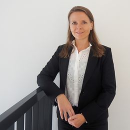 A woman in a blouse and jacket looks friendly into the camera.