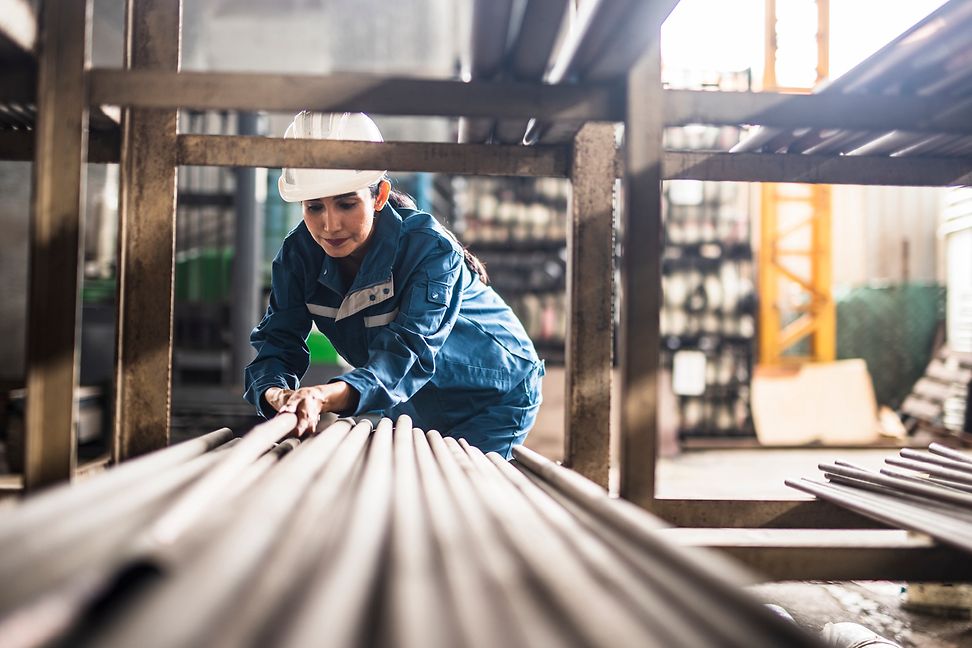 A person wearing a helmet and protective clothing is working with large pipes in an industrial hall.