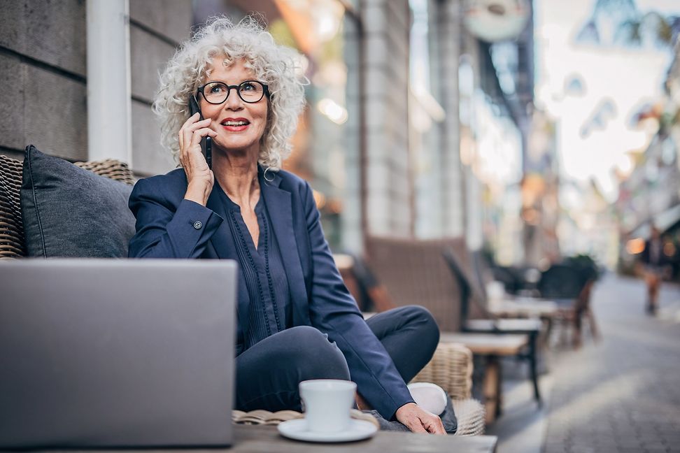 A businesswoman is sitting in a street café talking on the phone.